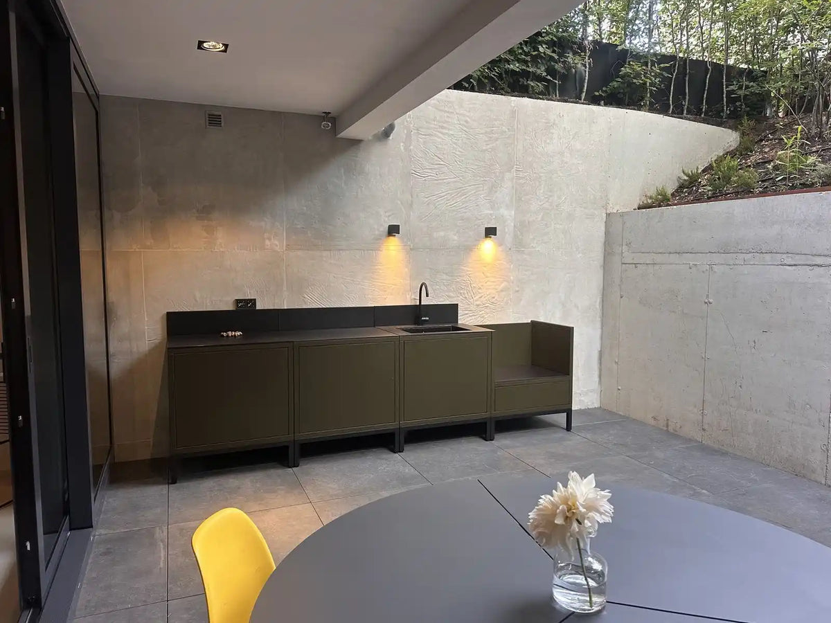Cocina exterior Kokko en color oliva instalada en casa de un cliente, terraza con vistas al jardín
