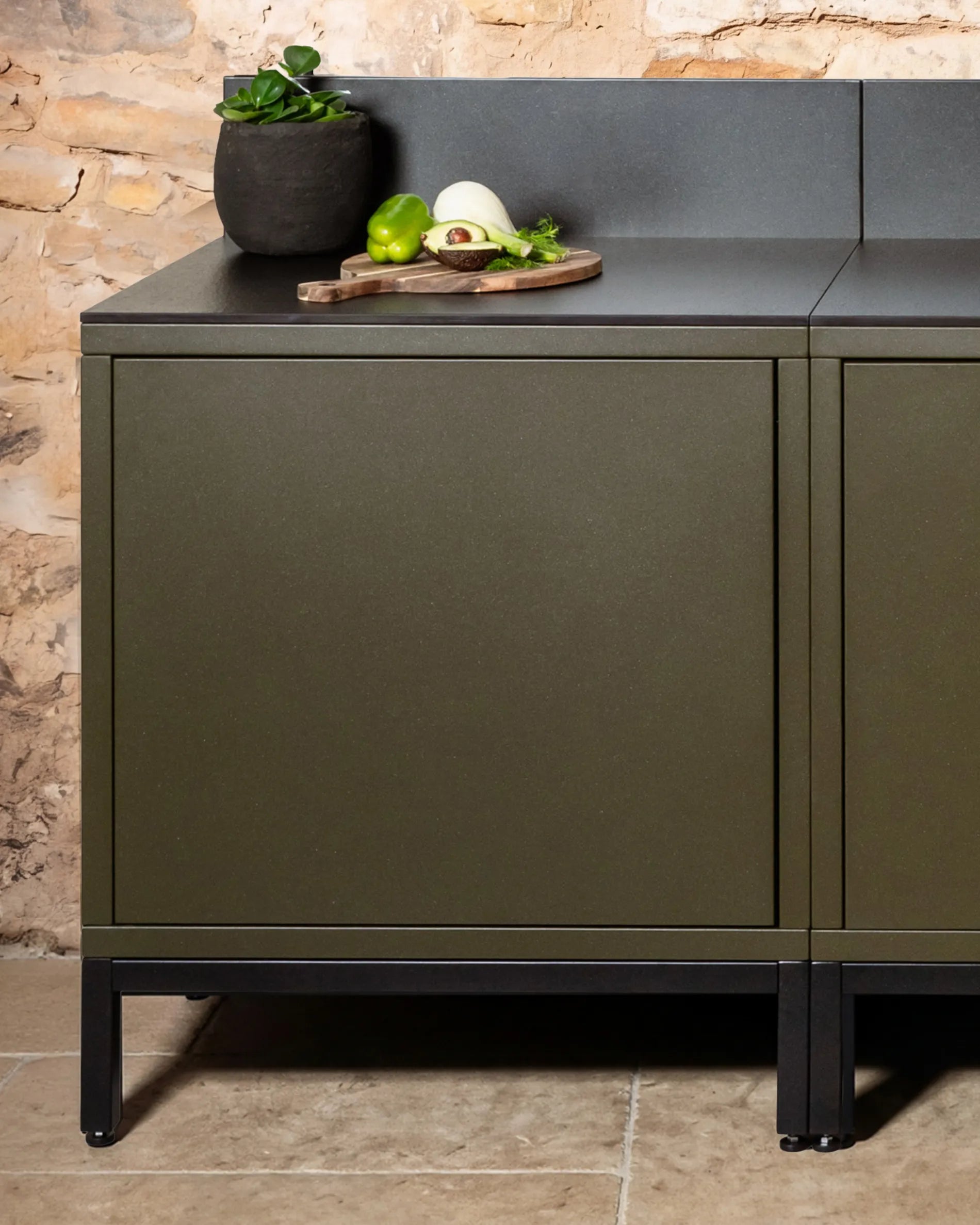 Estructura baja negra PILOTIS bajo módulos verde oliva, cocina exterior con encimera negra