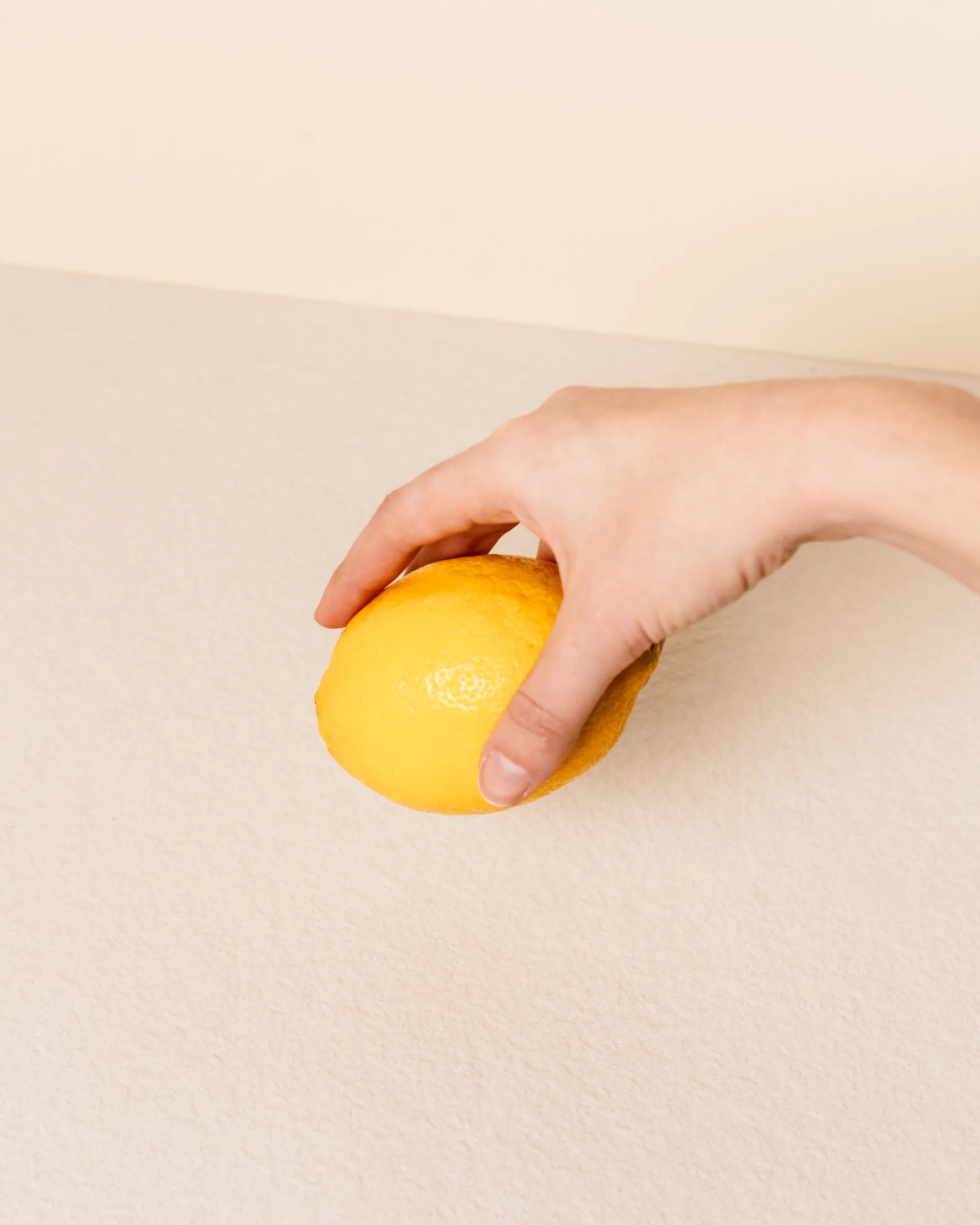 Mano sosteniendo un limón sobre la bandeja beige crema del módulo Classic PILOTIS, primer plano