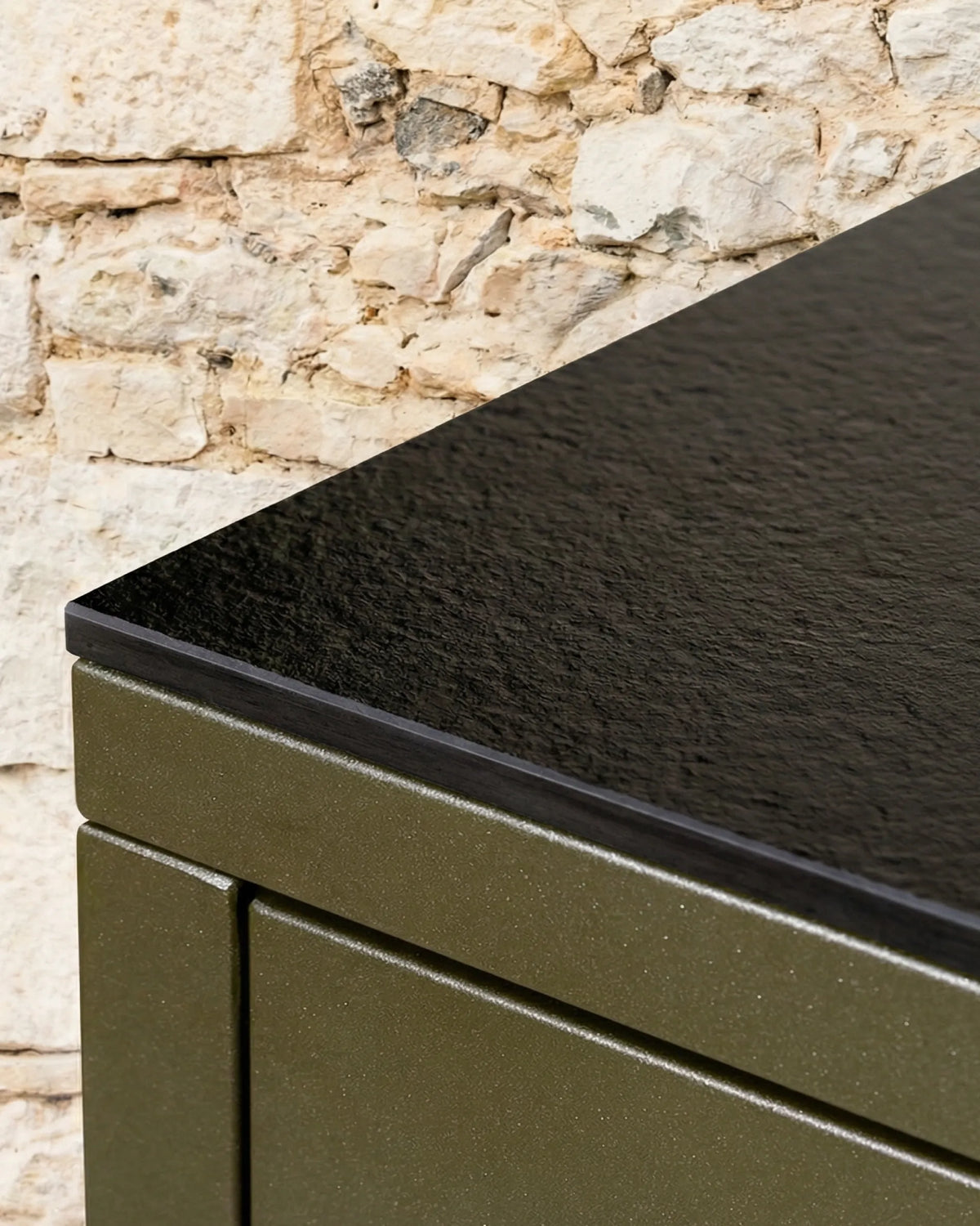 Unión en ángulo del tablero negro PILOTIS, primer plano del módulo verde oliva junto a una pared de piedra