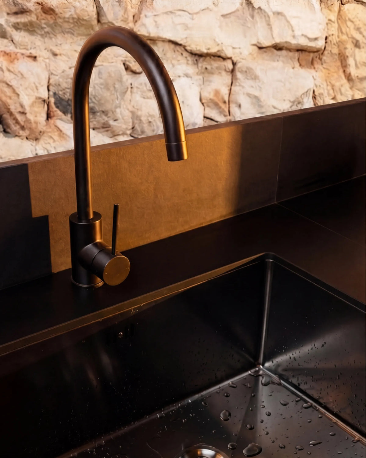 Primer plano del lavabo negro y grifo con acabado en bronce del módulo Fregadero PILOTIS