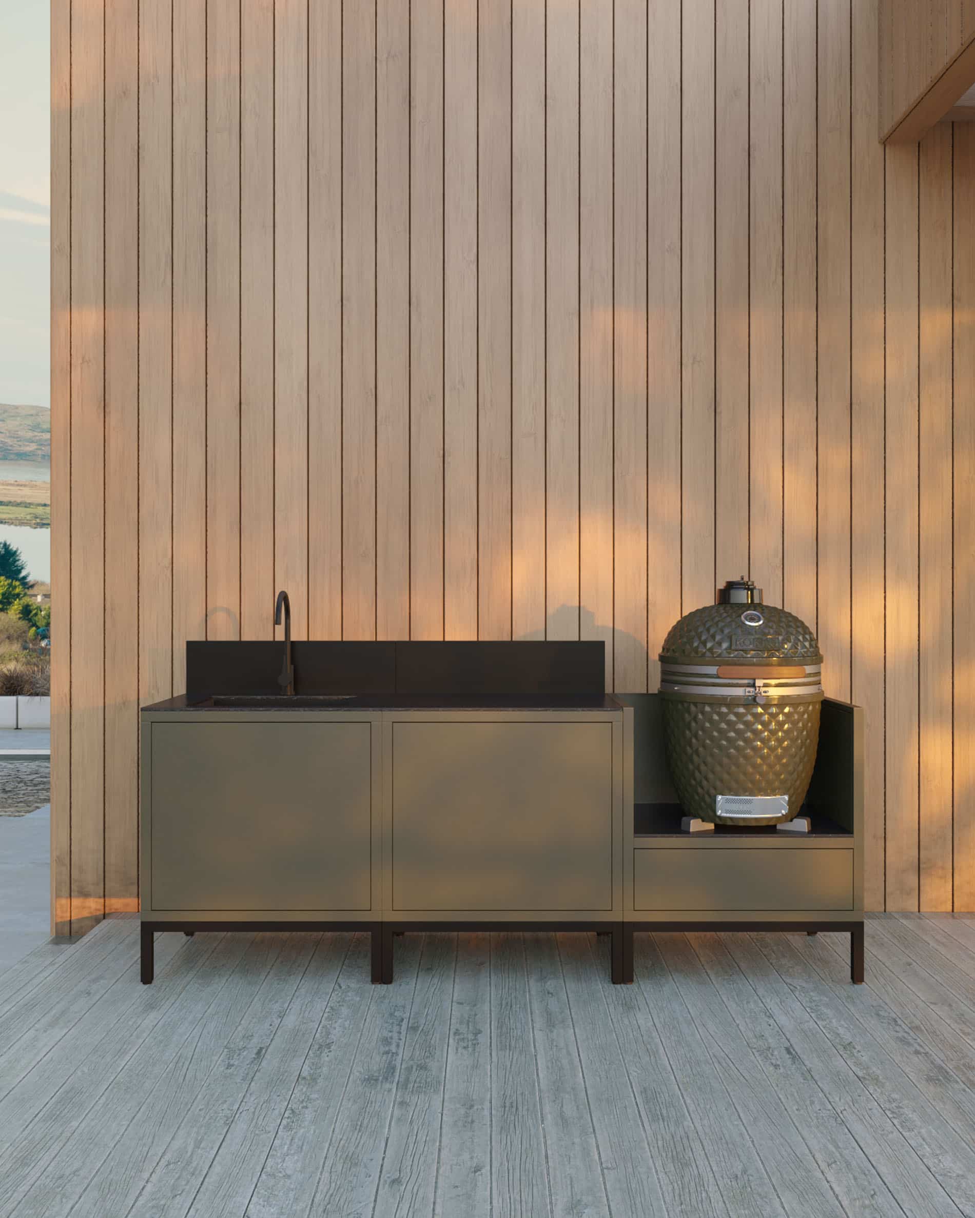 Cocina exterior pilotis de 3 módulos para kamado con fregadero integrado, mueble en color oliva con encimera y salpicadero a juego, fregadero con grifo a la izquierda, dos módulos de almacenamiento cerrados en el centro y kamado integrado en el módulo lateral derecho, estructura sobre patas negras, instalación en exterior junto a una pared revestida de madera.