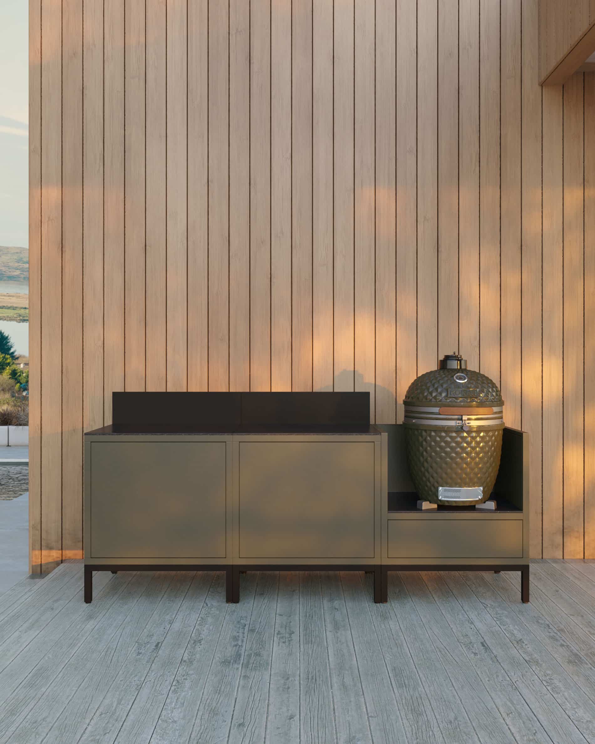 Cocina pilotis de 3 módulos para kamado, mueble en color verde oliva con encimera oscura y panel trasero a juego, dos módulos de almacenamiento cerrados a la izquierda y kamado integrado en el módulo lateral derecho, estructura sobre patas negras, instalación exterior junto a una pared de madera.