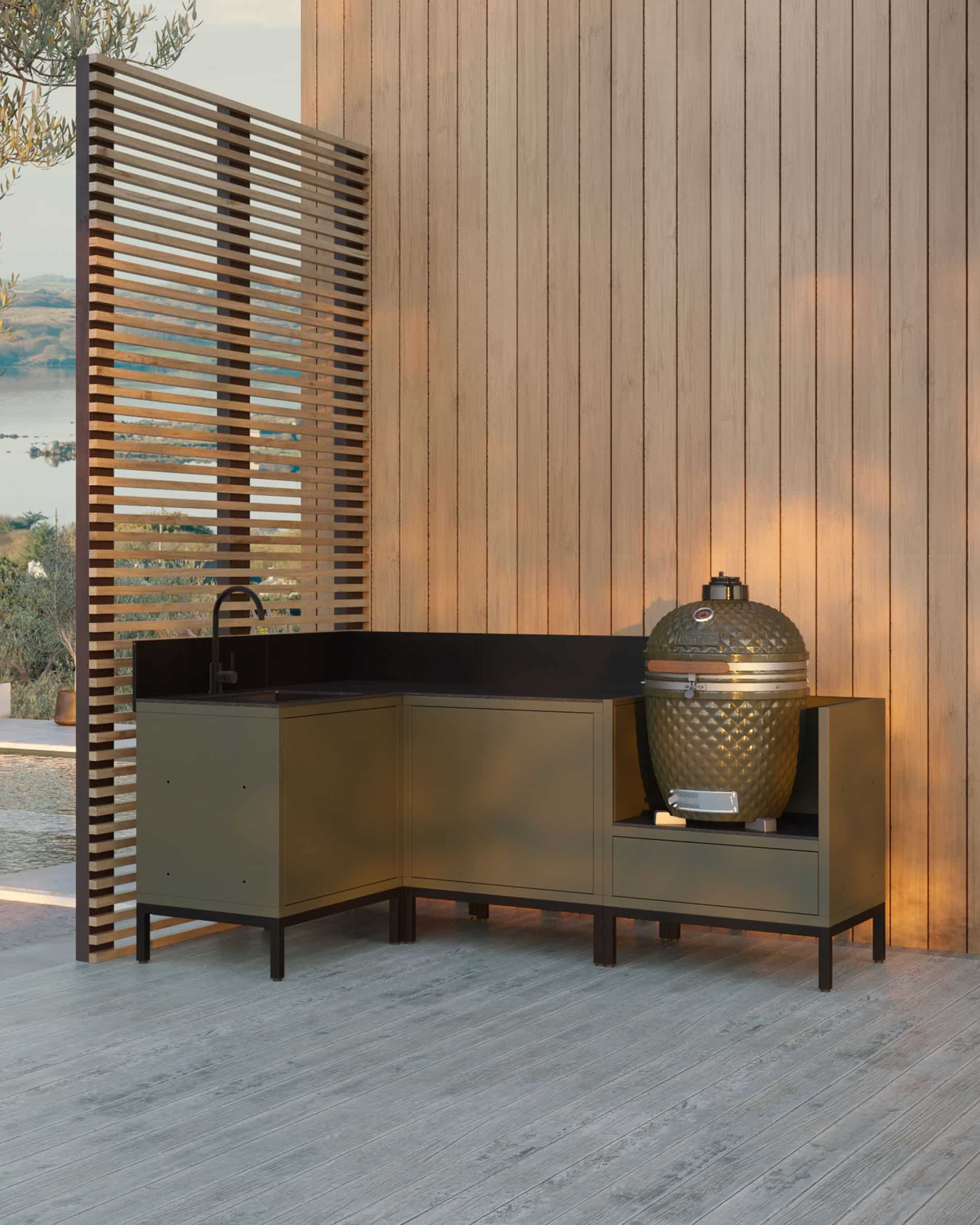 Cocina en esquina sobre pilotes color oliva, compuesta por cuatro módulos con fregadero integrado, encimera negra y espacio dedicado al kamado, instalada en una terraza de madera junto a un revestimiento vertical.