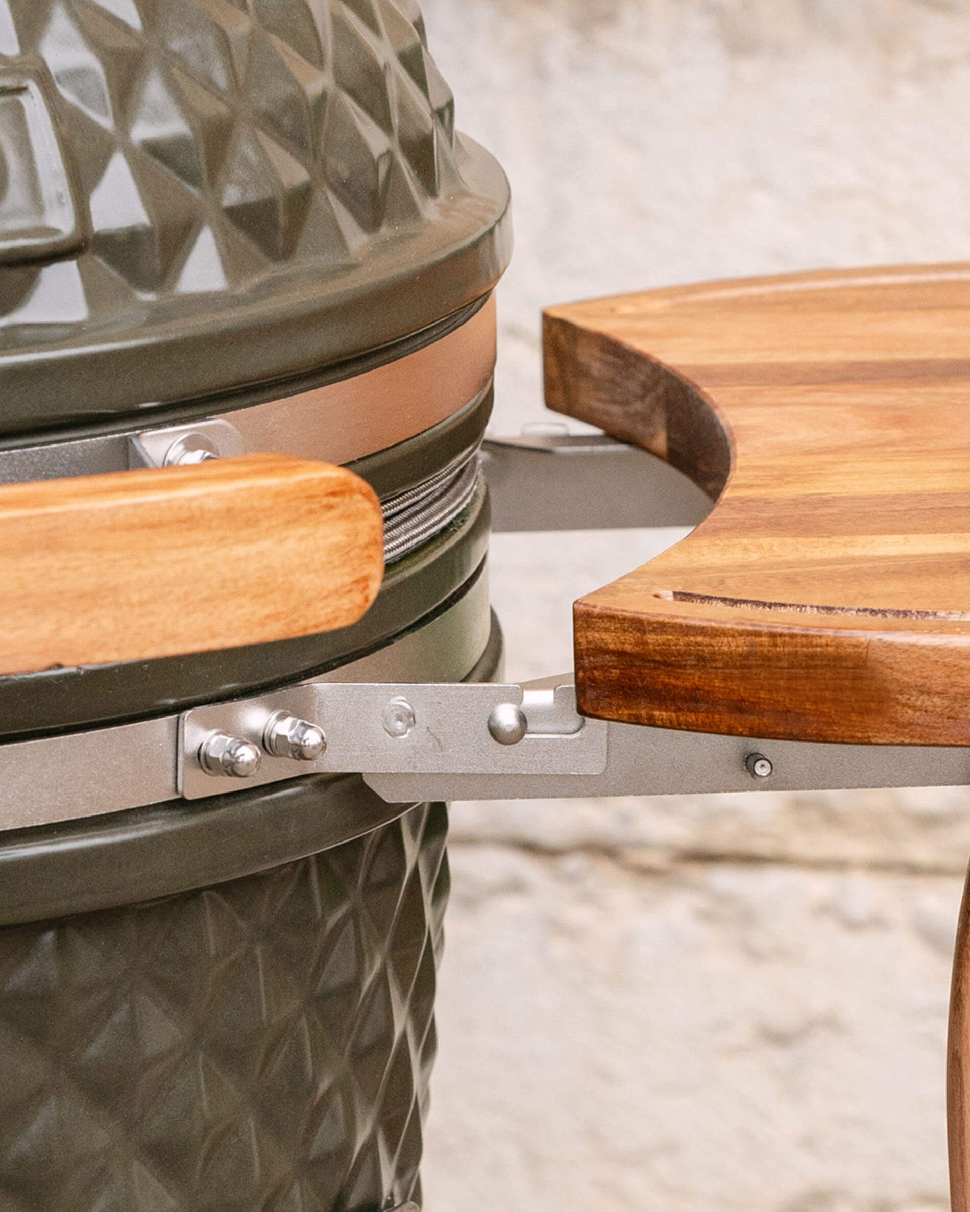 Primer plano de la fijación metálica que une la bandeja lateral de madera al kamado, mostrando el sistema de enganche y la tornillería.