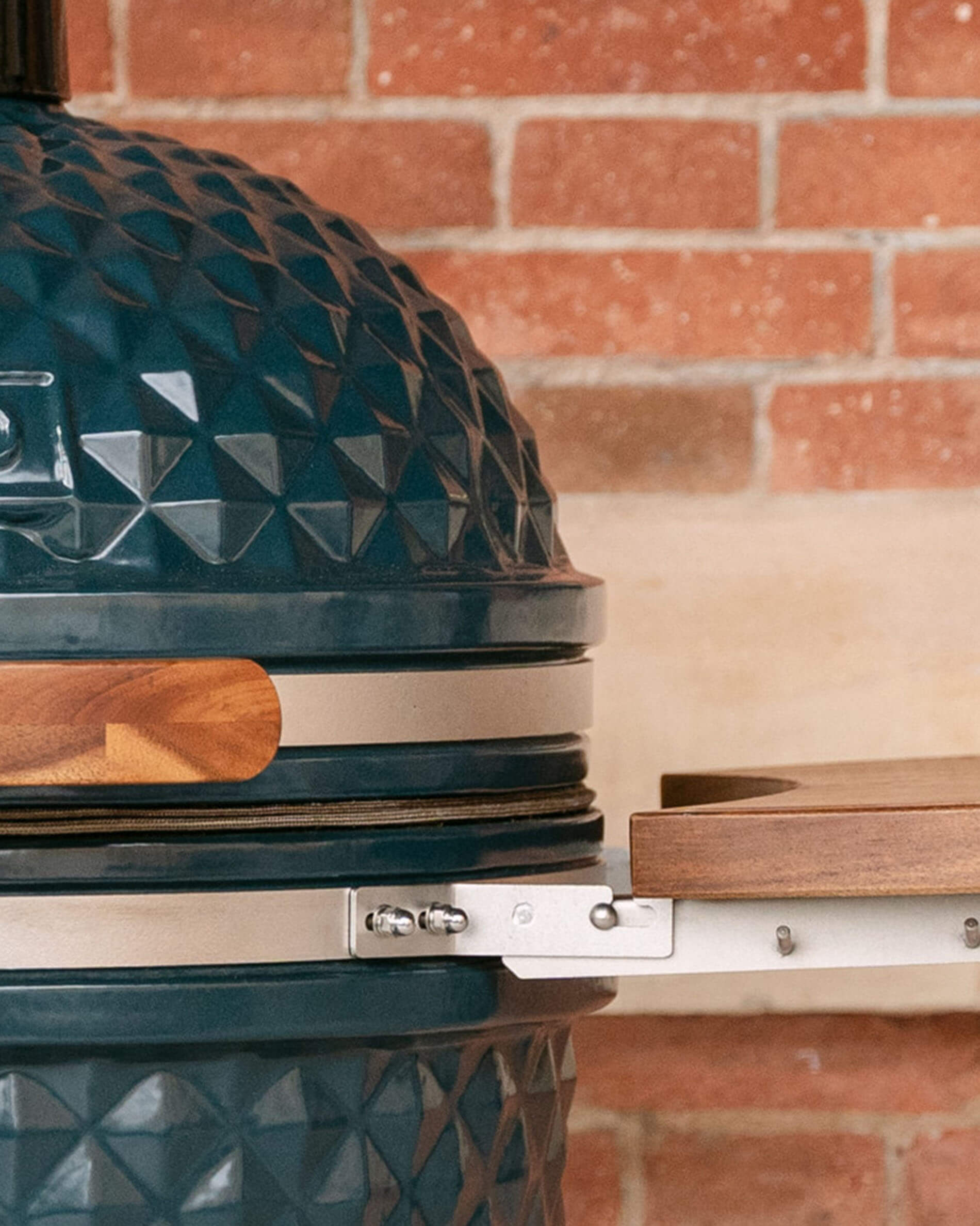 Detalle de las fijaciones metálicas que unen una bandeja lateral de madera al cuerpo del kamado, con tornillería visible y junta a la vista.