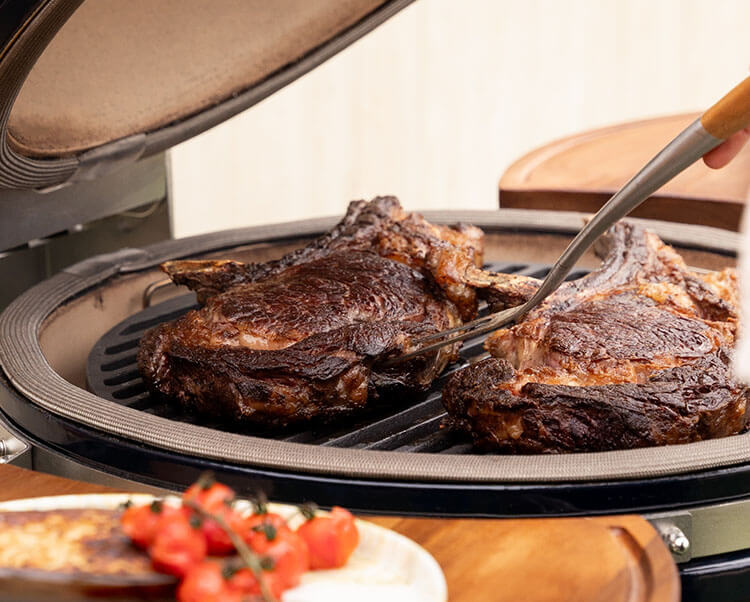 Cuisson directe sur kamado Kokko XL 22 pouces, illustrant la saisie des aliments sur la grille en inox.