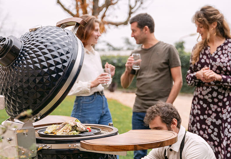 Grupo de amigos reunidos alrededor de un kamado Kokko durante una comida al aire libre, ilustrando un momento de compartir y de convivialidad.