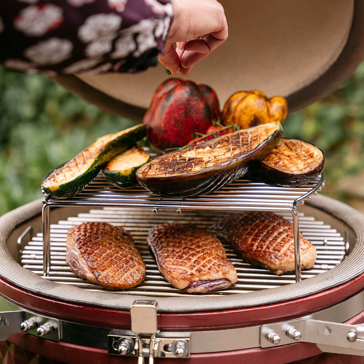 Cuisson en deux niveaux dans un kamado Kokko avec magrets de canard saisis sur la grille inférieure et légumes grillés sur la grille surélevée, illustrant la polyvalence de cuisson.