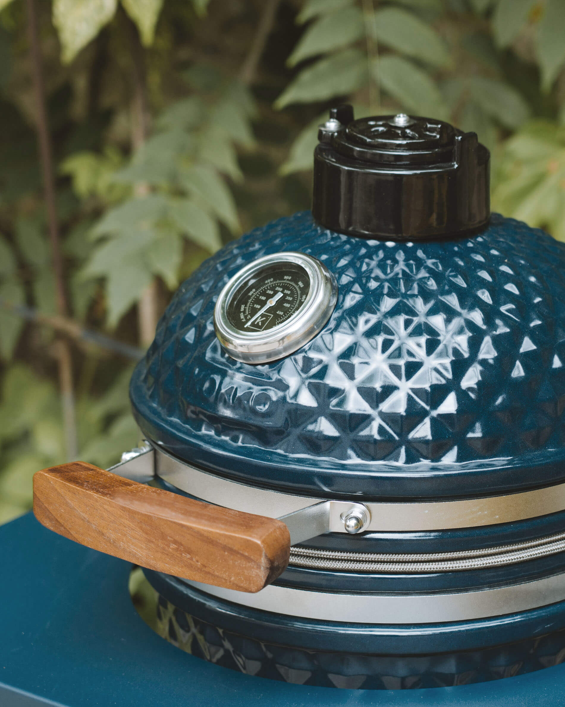 Detalle de la tapa de un kamado Kokko color océano con termómetro integrado y asa de madera.