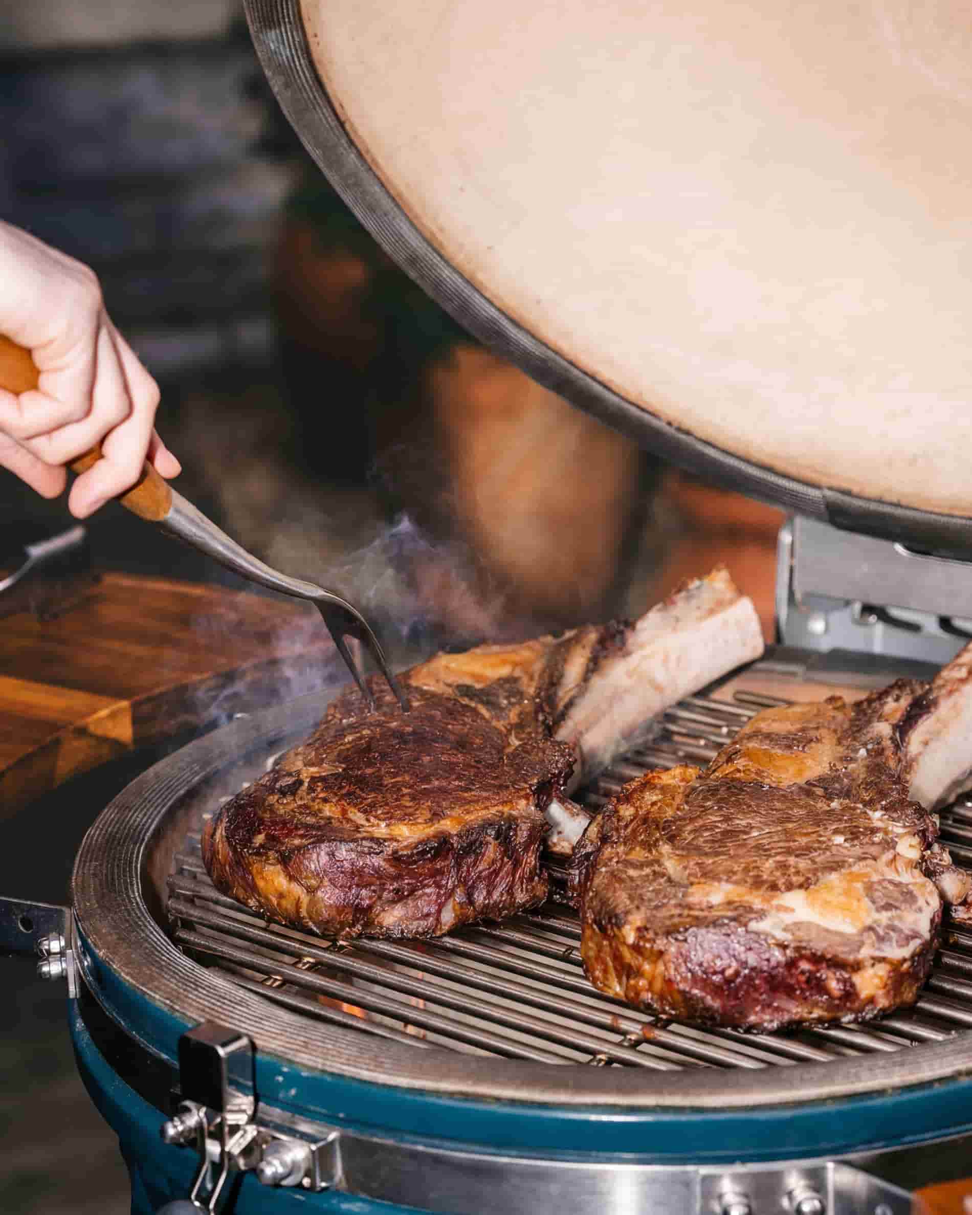 Cocción de carne sobre la parrilla de un kamado Kokko XL de 22 pulgadas, con la tapa abierta.