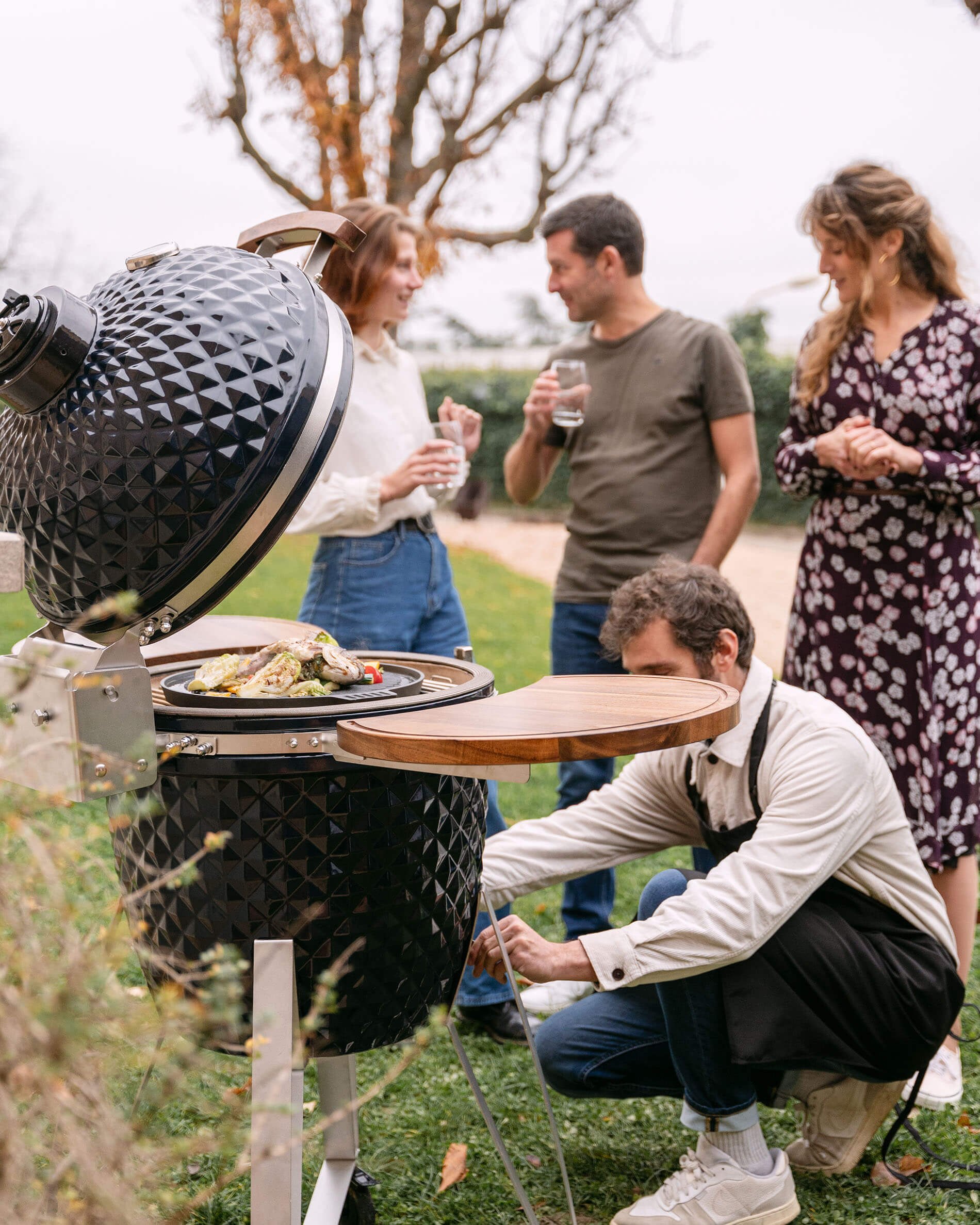 Kamado Kokko de 22 pulgadas en cerámica azul marino utilizado durante un momento de convivencia al aire libre.
