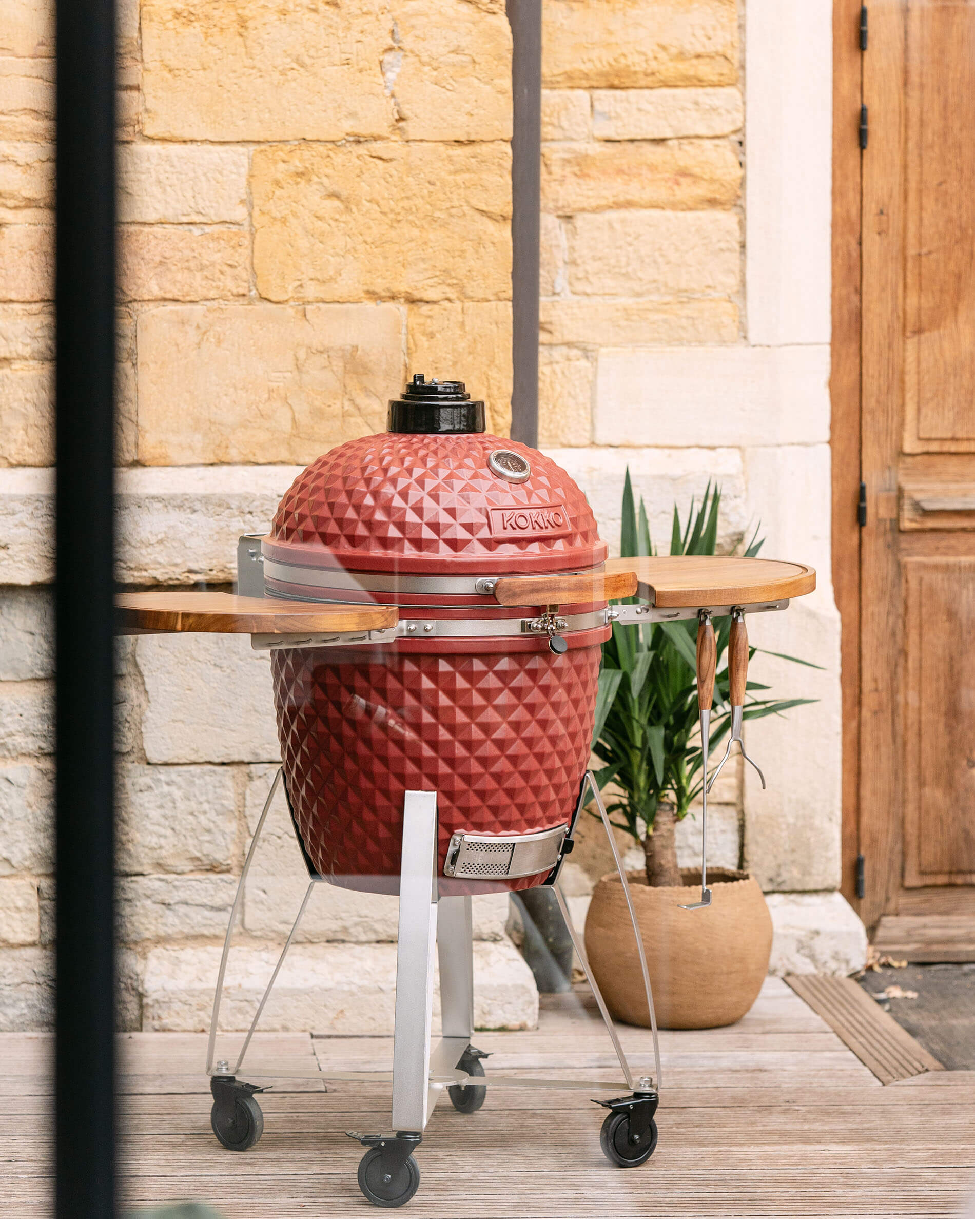 Kamado Kokko XL de 22 pulgadas en cerámica rojo óxido, instalado sobre carro en exterior.