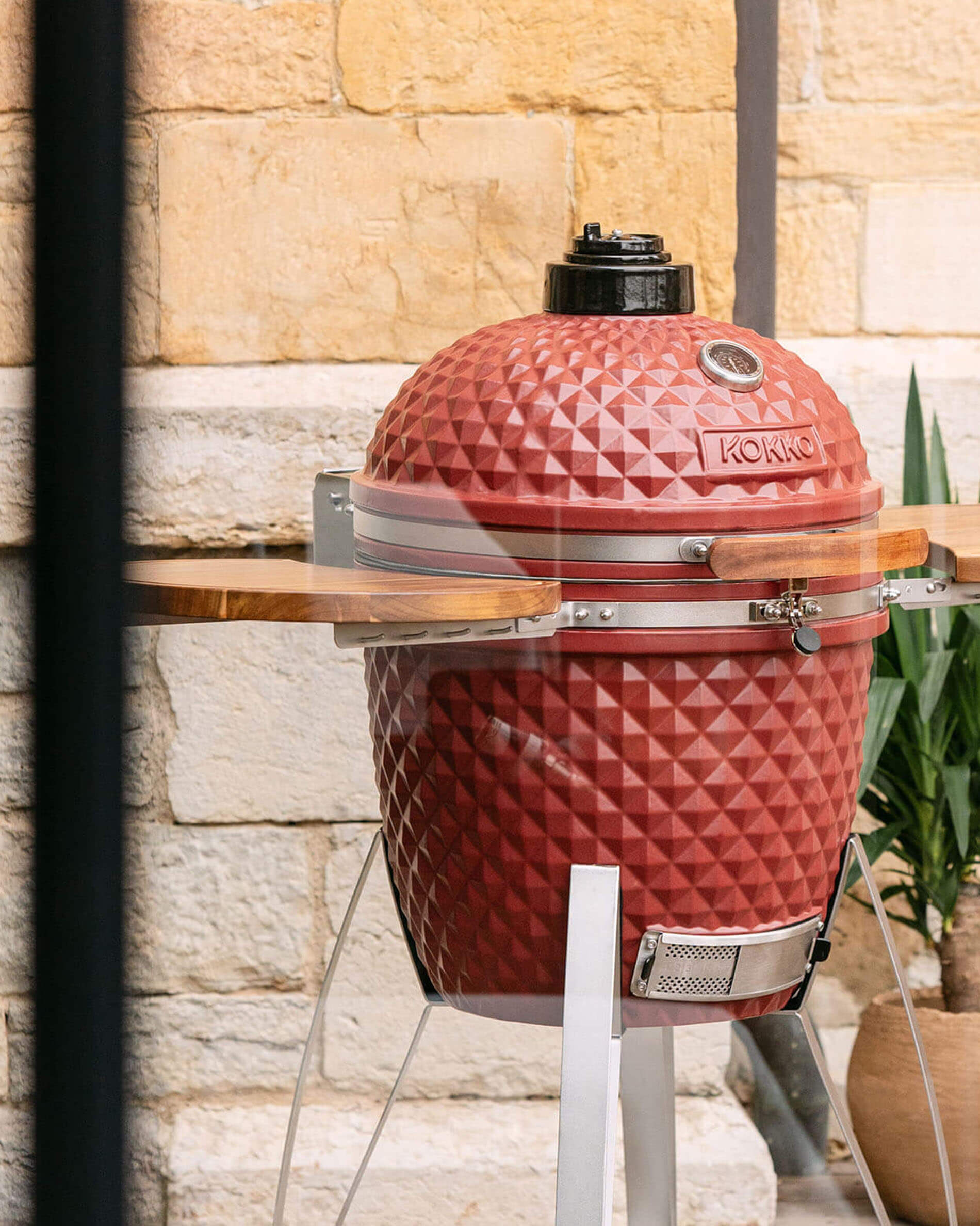 Kamado Kokko de 22 pulgadas en color rojo óxido, presentado solo en exterior.