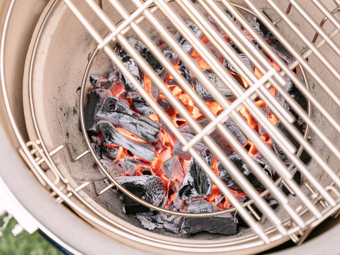 Carbón de leña incandescente en la cuba de cerámica de un kamado Kokko, con brasas rojas visibles bajo la parrilla de acero inoxidable, ilustrando el aumento de temperatura y el control preciso de la cocción al fuego de leña.