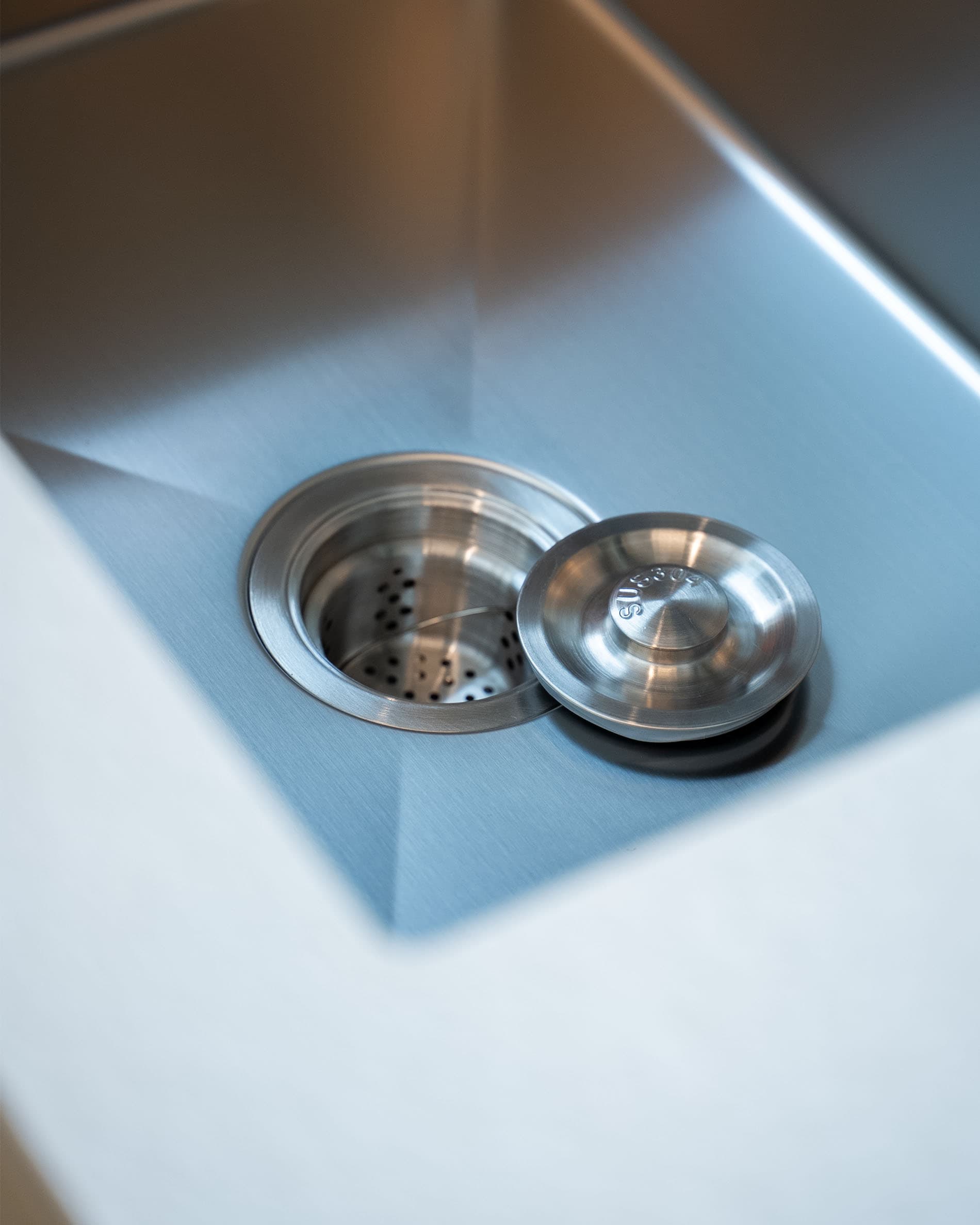 Detalle del desagüe del fregadero de una cocina sobre pilotes, mostrando la cubeta de acero inoxidable y el sistema de evacuación integrado.