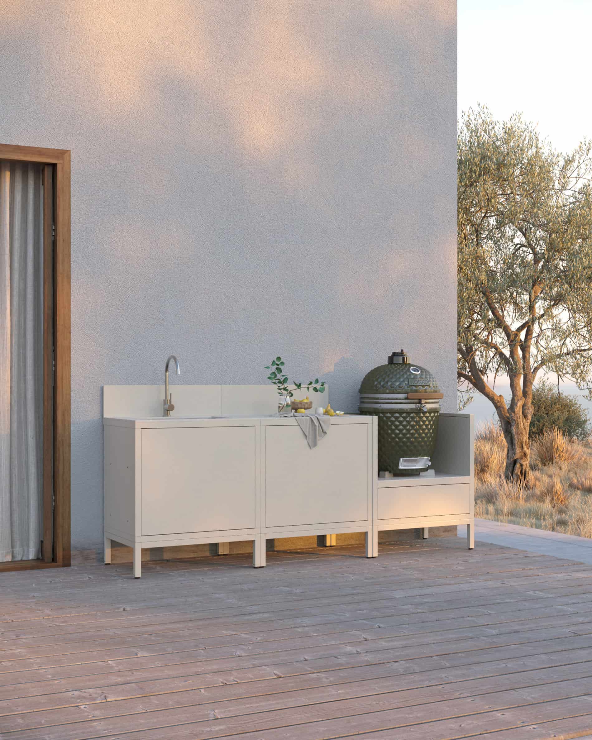 Cocina sobre pilotes en color crema, compuesta por tres módulos con fregadero integrado, superficie de trabajo clara y espacio dedicado al kamado, instalada en una terraza de madera.