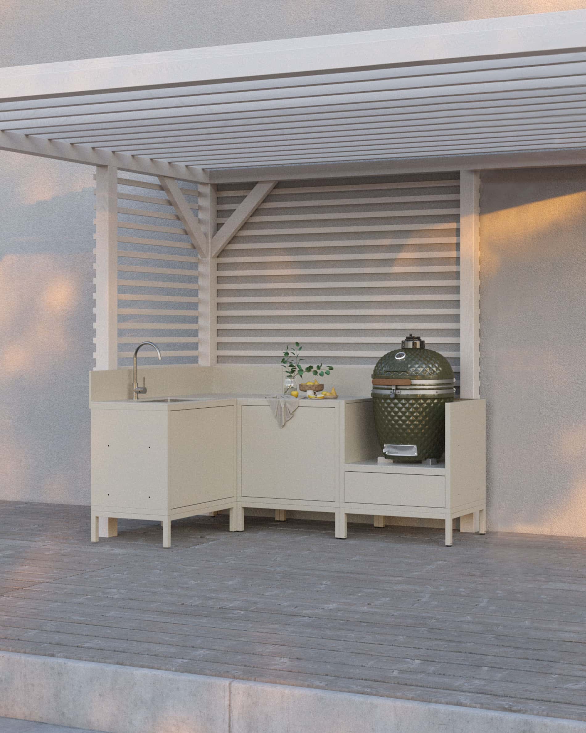 Cocina pilotis en color crema compuesta por cuatro módulos con esquina y fregadero, encimera continua y espacio dedicado al kamado, instalada bajo una pérgola blanca sobre terraza de madera.