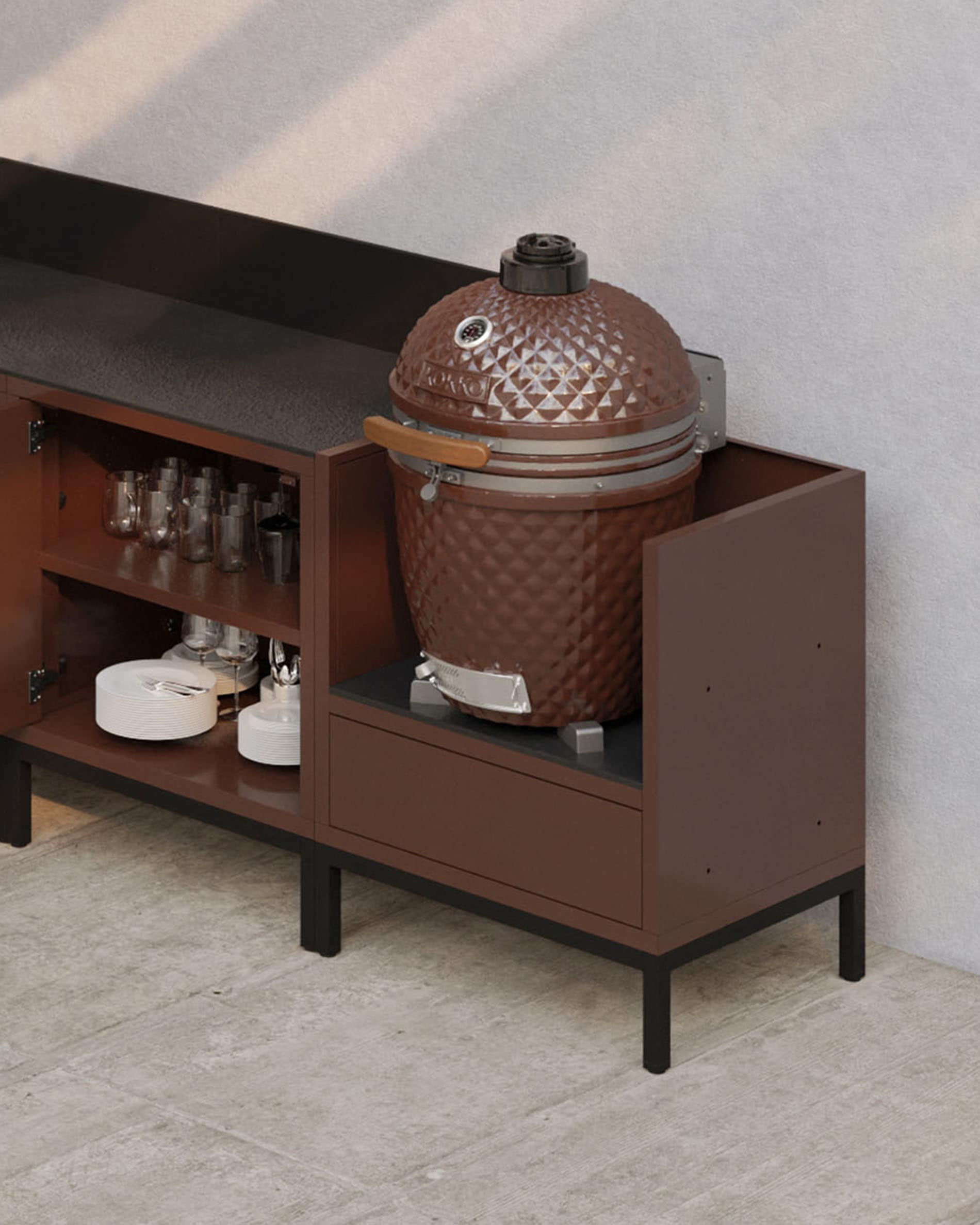 Cocina modular sobre pilotes en color óxido, con encimera oscura, estantes abiertos y módulo diseñado para integrar un kamado.