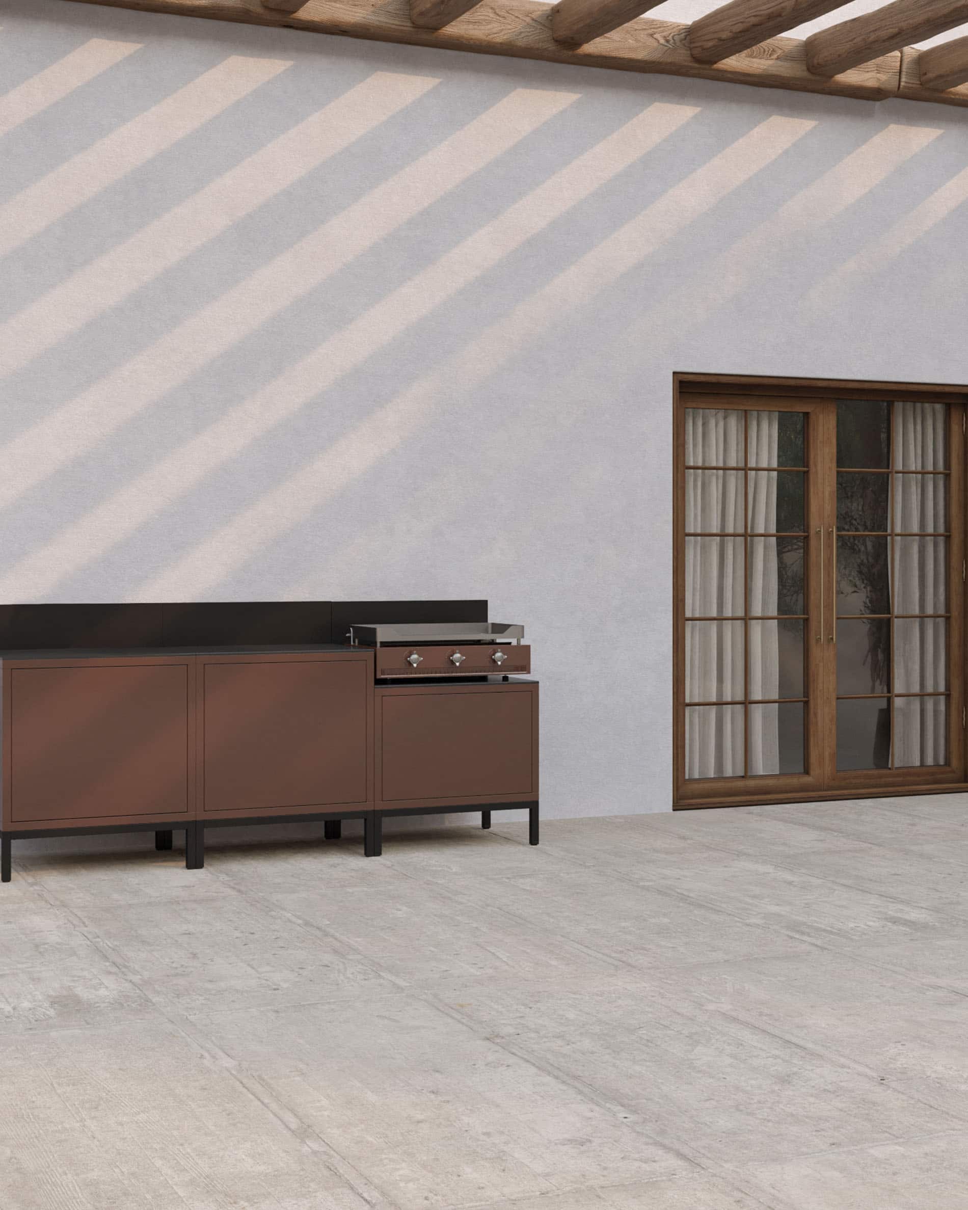 Cocina exterior sobre pilotes con plancha integrada, muebles en color marrón óxido, almacenaje cerrado y encimera oscura, instalada en una terraza cubierta.