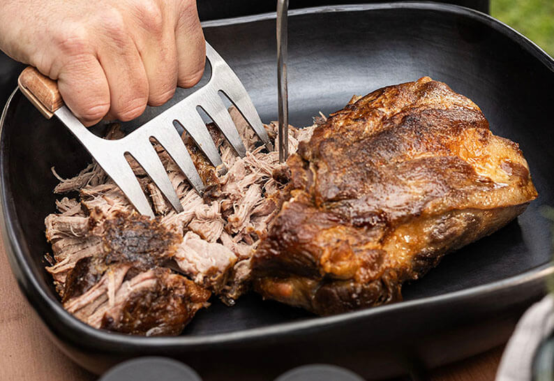 Cerdo desmenuzado cocinado en el kamado Kokko, desmenuzado con un par de garras sobre la parrilla.