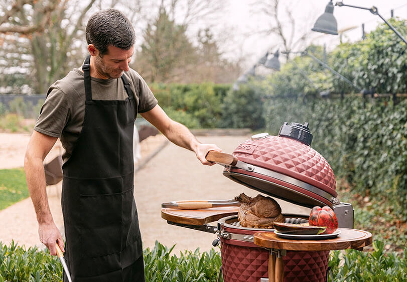 Asado de un rosbif en un kamado Kokko rojo, con la tapa abierta y manipulación de los alimentos al aire libre.